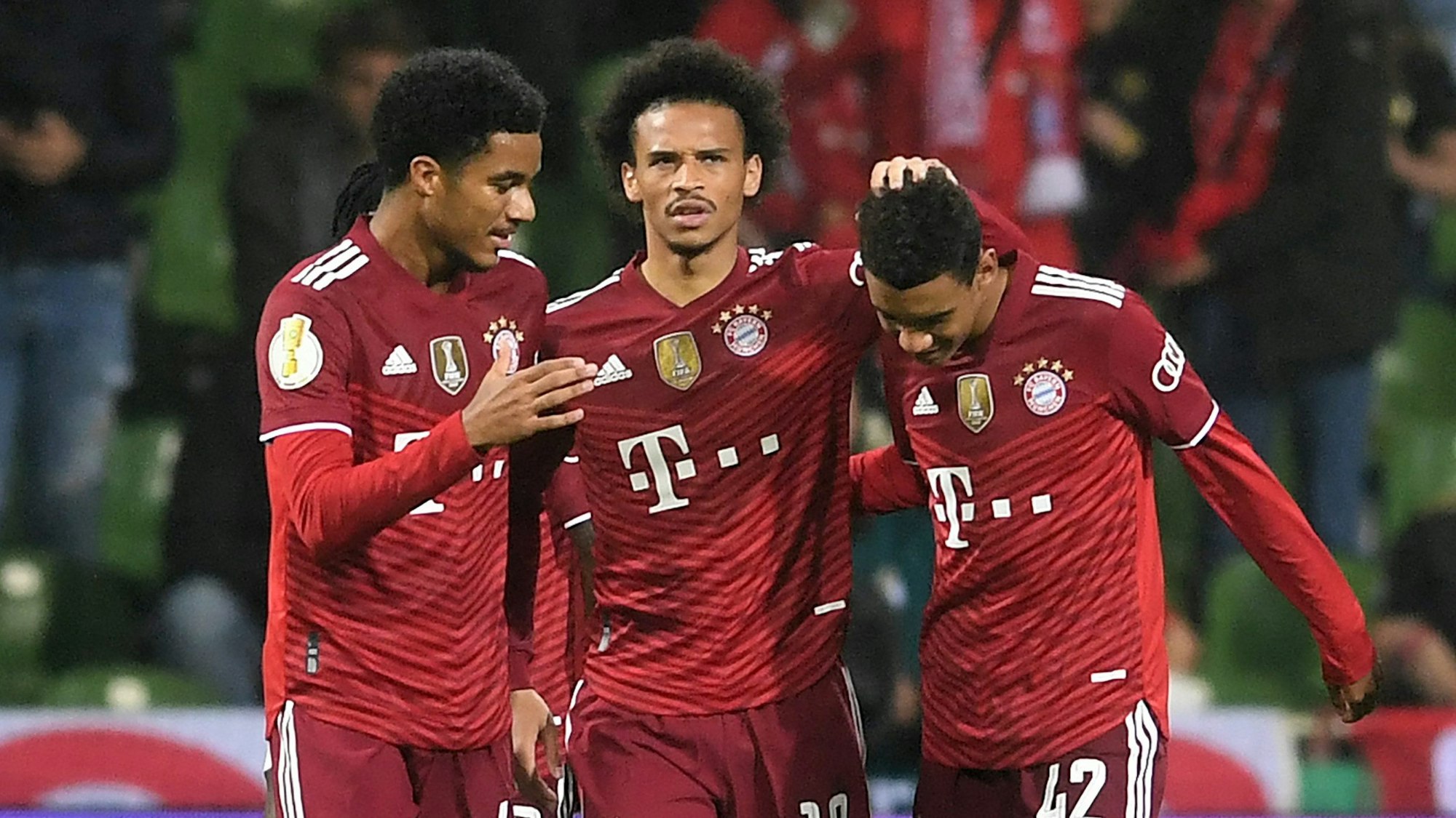 Bayerns Malik Tillmann (l) und Leroy Sane (M) freuen sich mit dem Torschützen zum 0:7 Jamal Musiala.