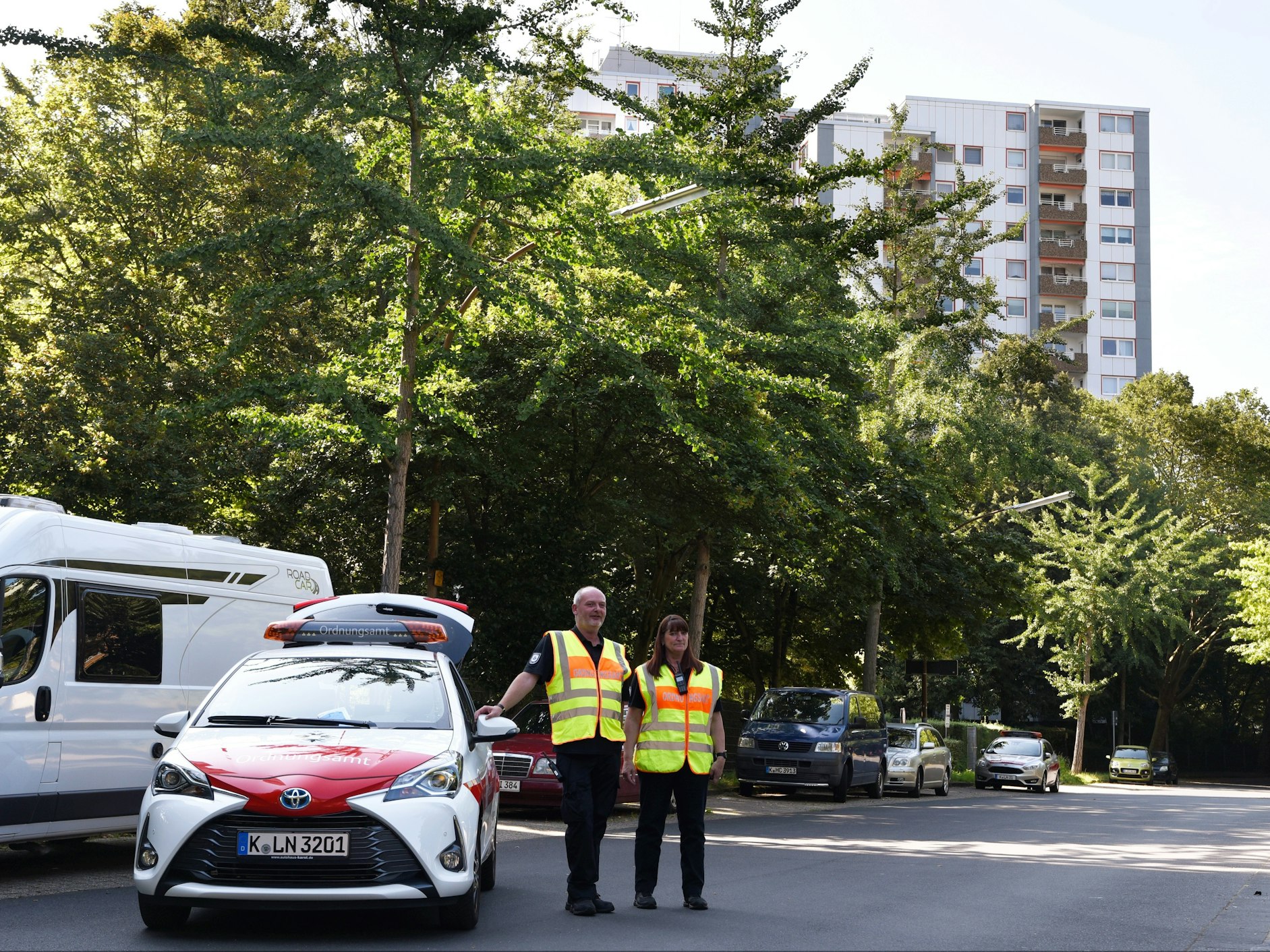 Zwei Personen in Warnwesten stehen vor einem Hochhaus.
