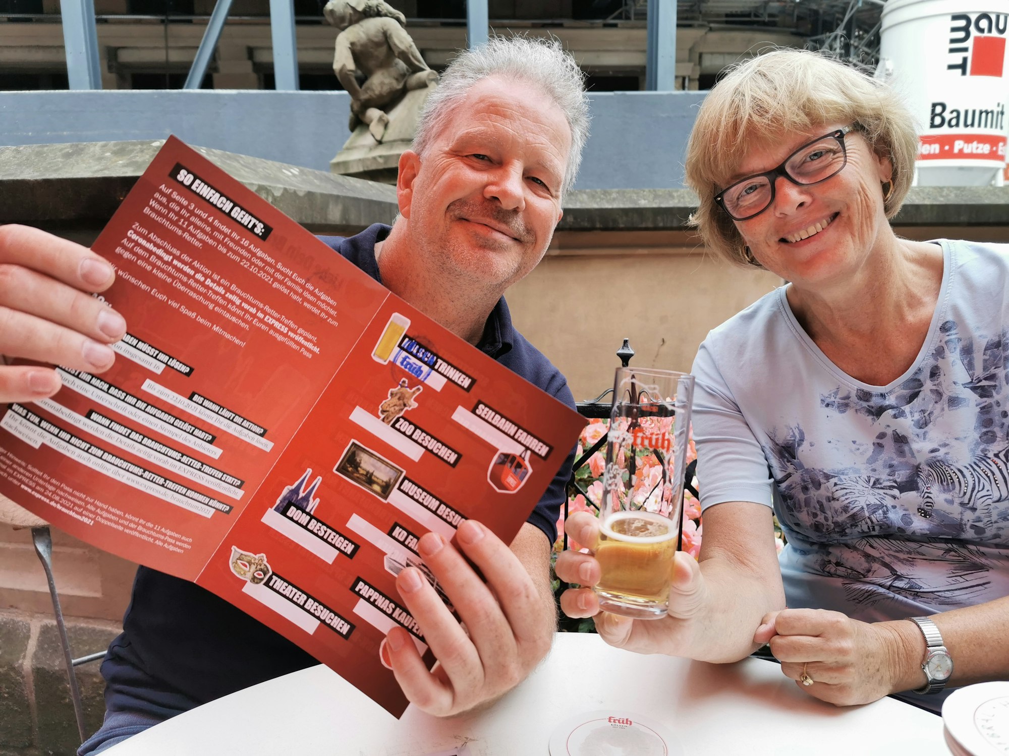 Hildegard aus Bornheim und EXPRESS-Reporter Oliver Meyer halten den Brauchtums-Pass in die Kamera und trinken Kölsch.