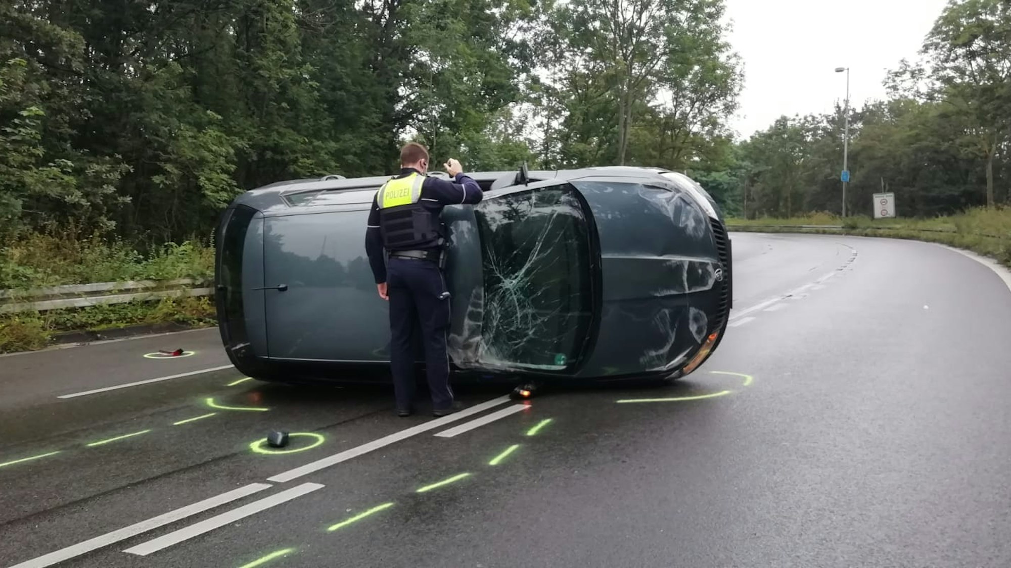 Ein stark beschädigtes Auto liegt auf der Seite auf einer Straße. Davor steht ein Polizist.