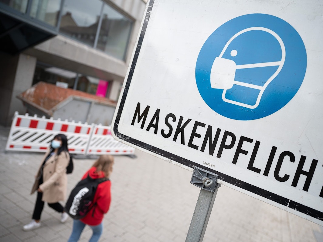 Zwei Passantinnen gehen in der Fußgängerzone hinter einem Schild vorbei, auf dem «Maskenpflicht» steht.