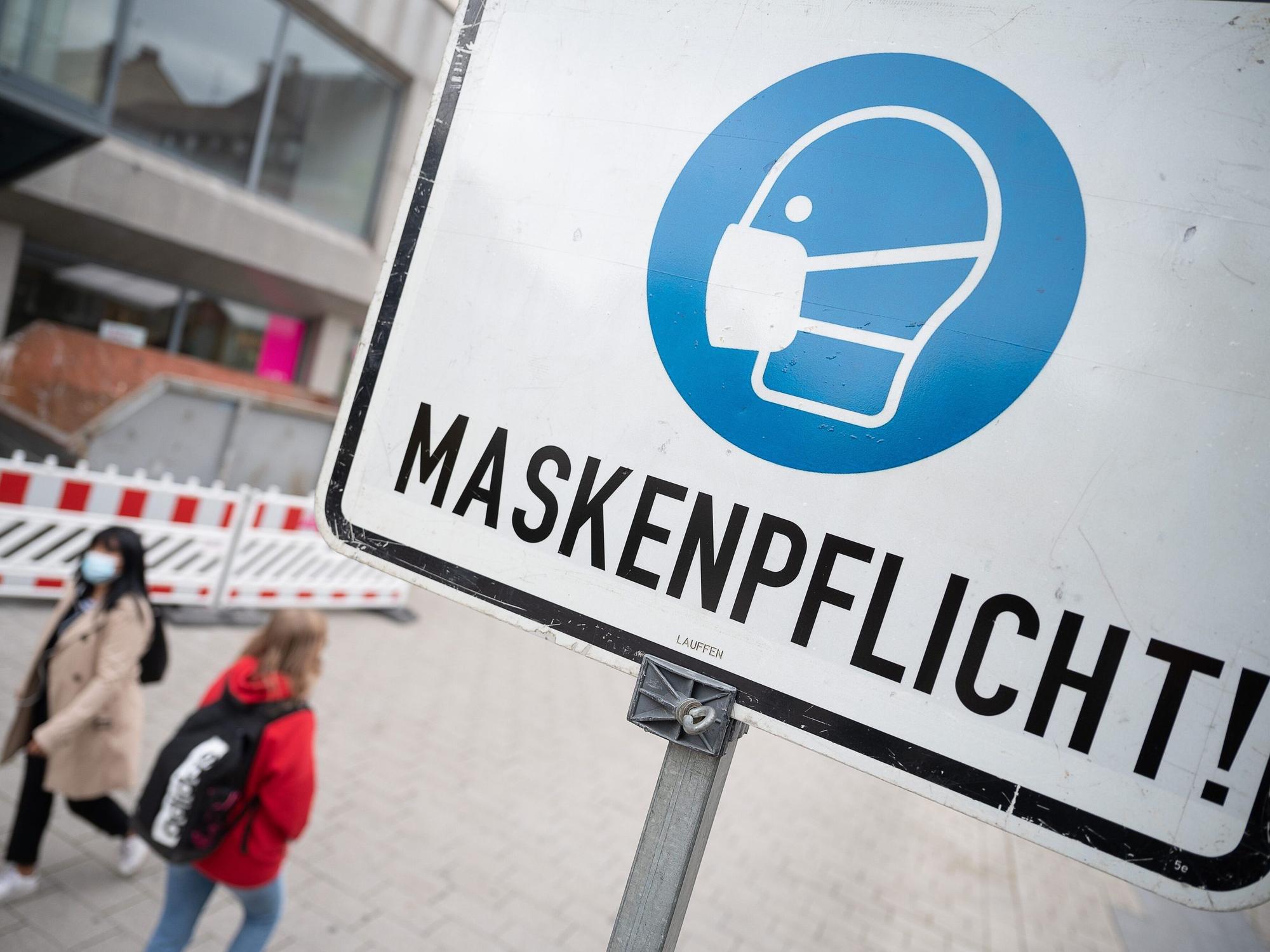 Zwei Passantinnen gehen in der Fußgängerzone hinter einem Schild vorbei, auf dem «Maskenpflicht» steht.