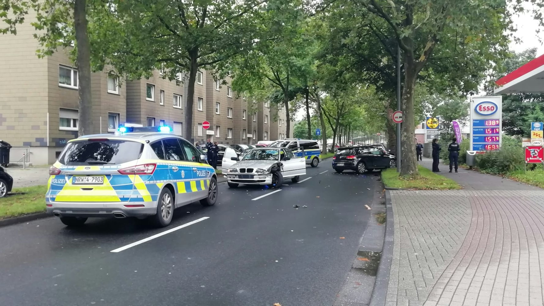 Zwei demolierte Autos sowie zwei Polizeifahrzeuge stehen auf der Straße.