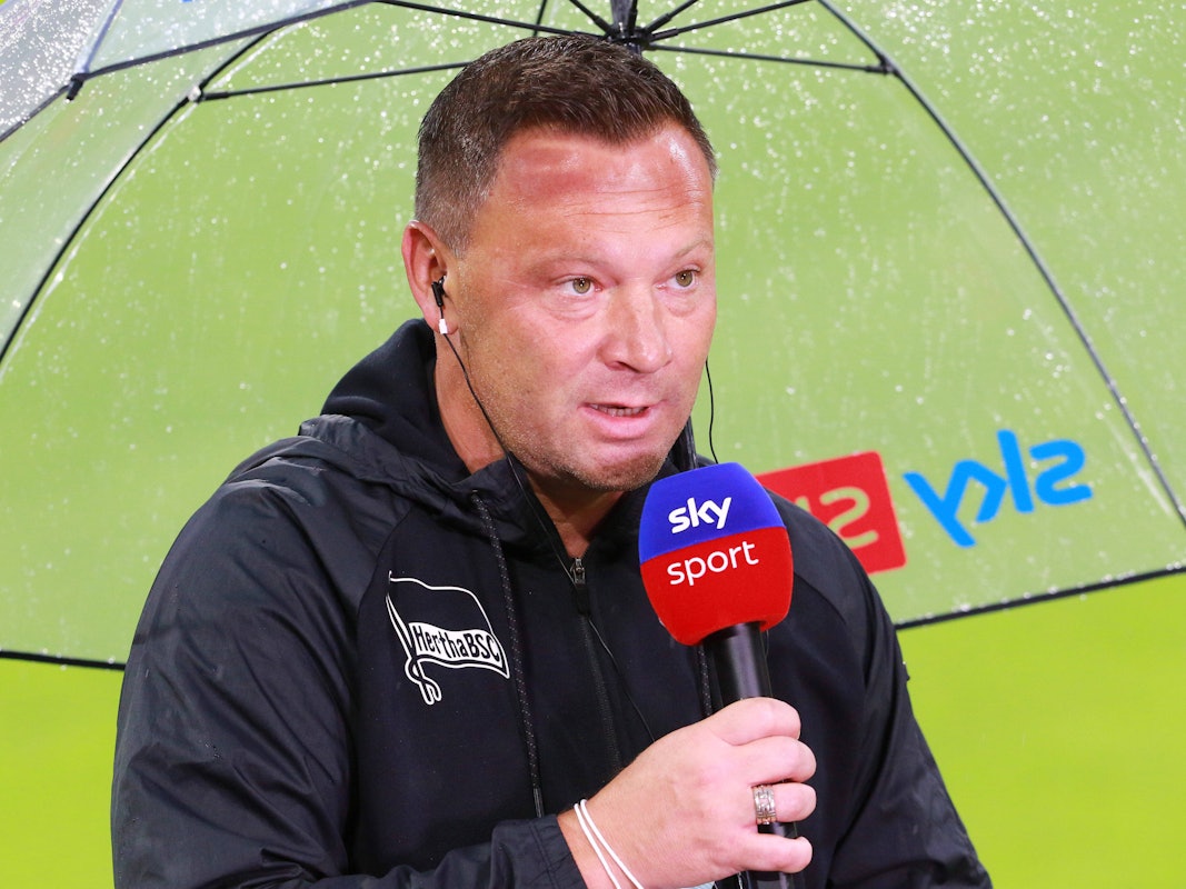Pal Dardai steht mit einem Mikro unter einem Regenschirm.