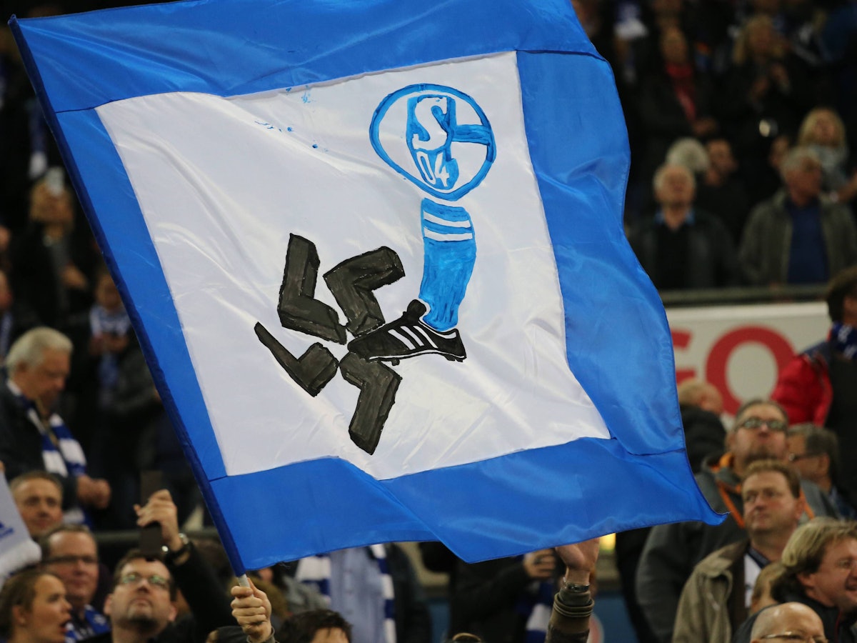 Auf einer Fahne ist ein Schalke-Wappen und ein Fuß zu sehen. Der Fuß zertritt ein Hakenkreuz.