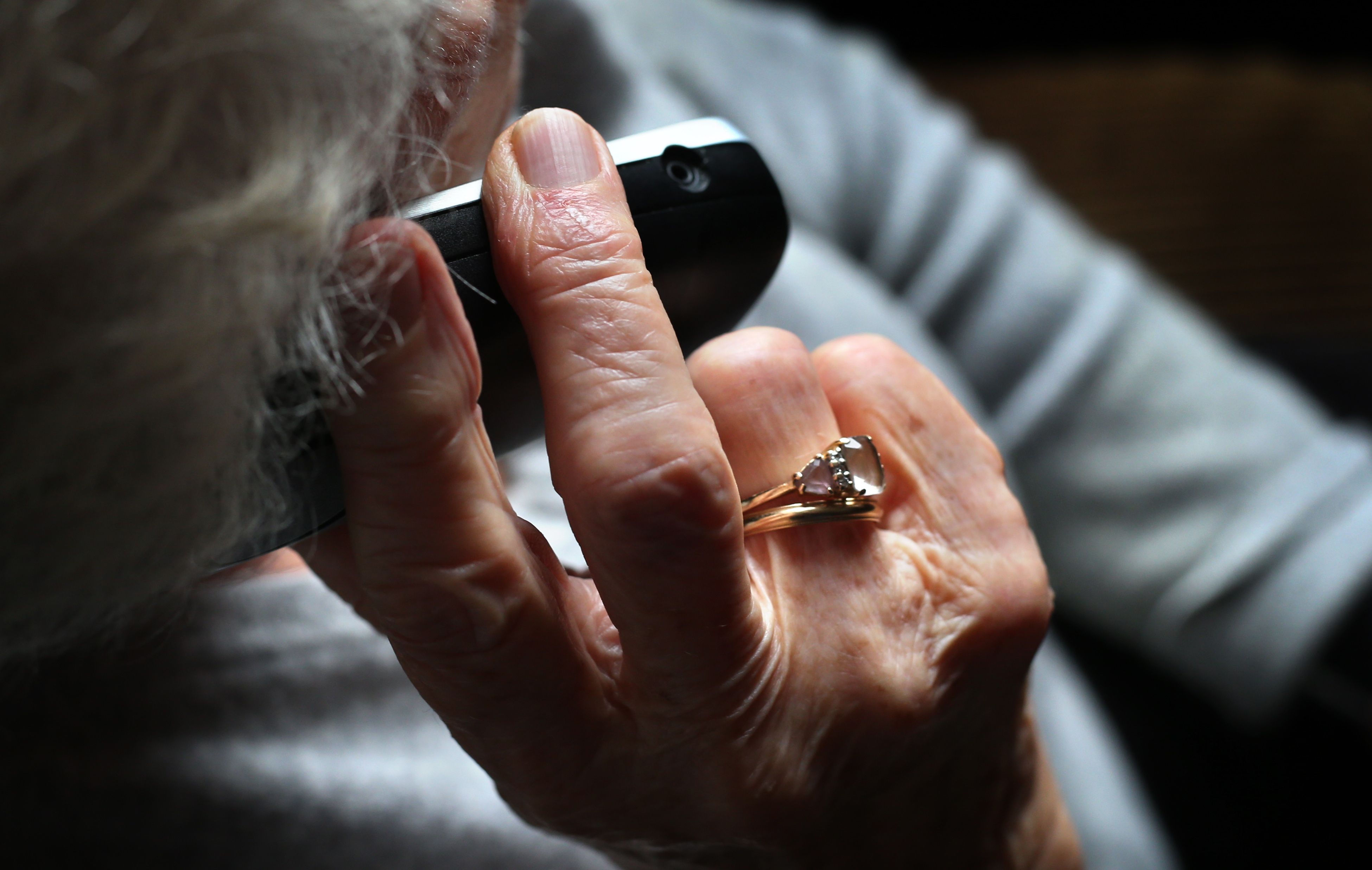 Eine ältere Frau, die einen wertvollen Ring am Finger trägt, telefoniert mit einem schnurlosen Festnetztelefon.