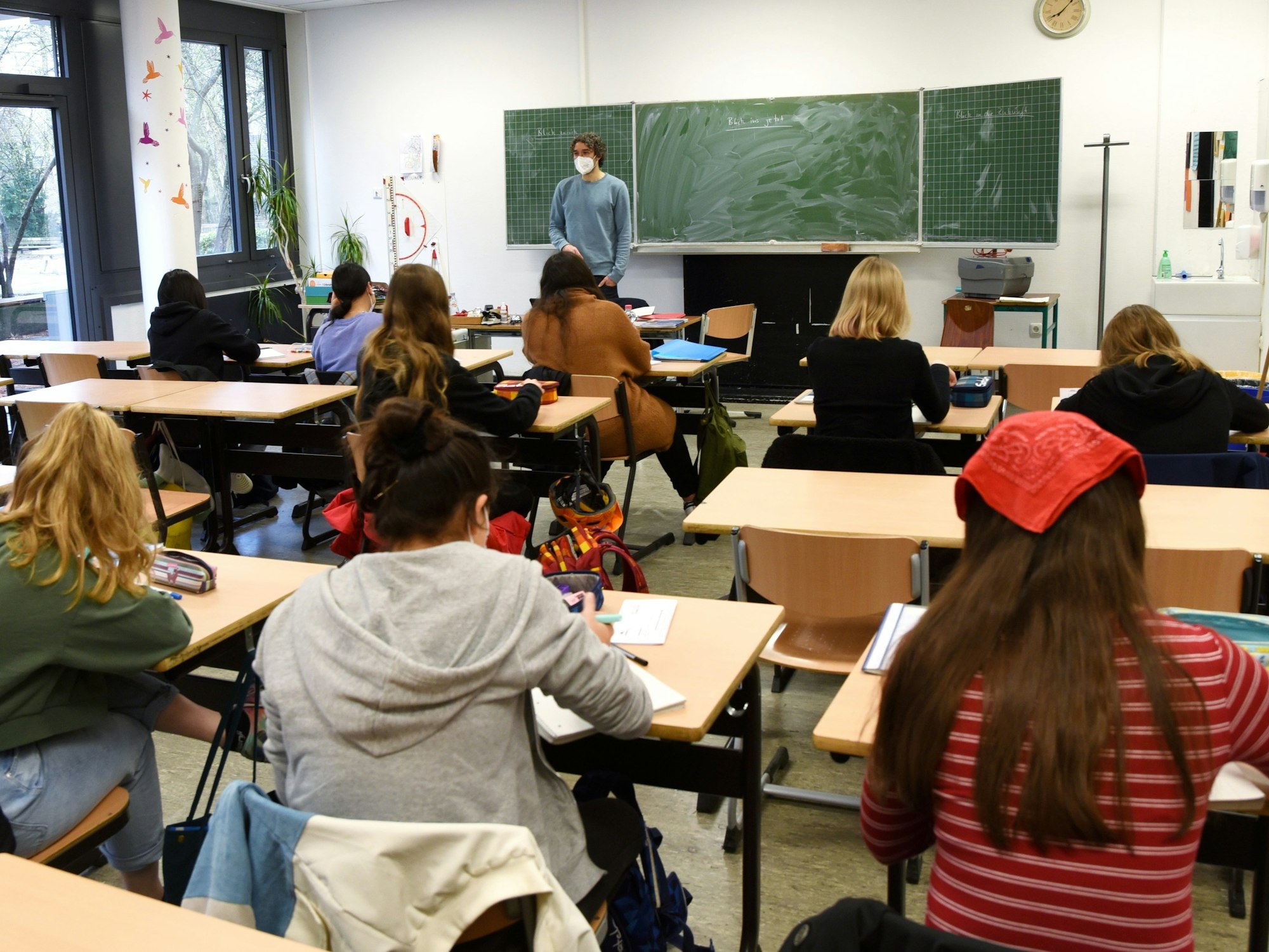 Schüler und Schülerinnen sitzen an ihren Tischen, schreiben und hören dem Lehrer zu.
