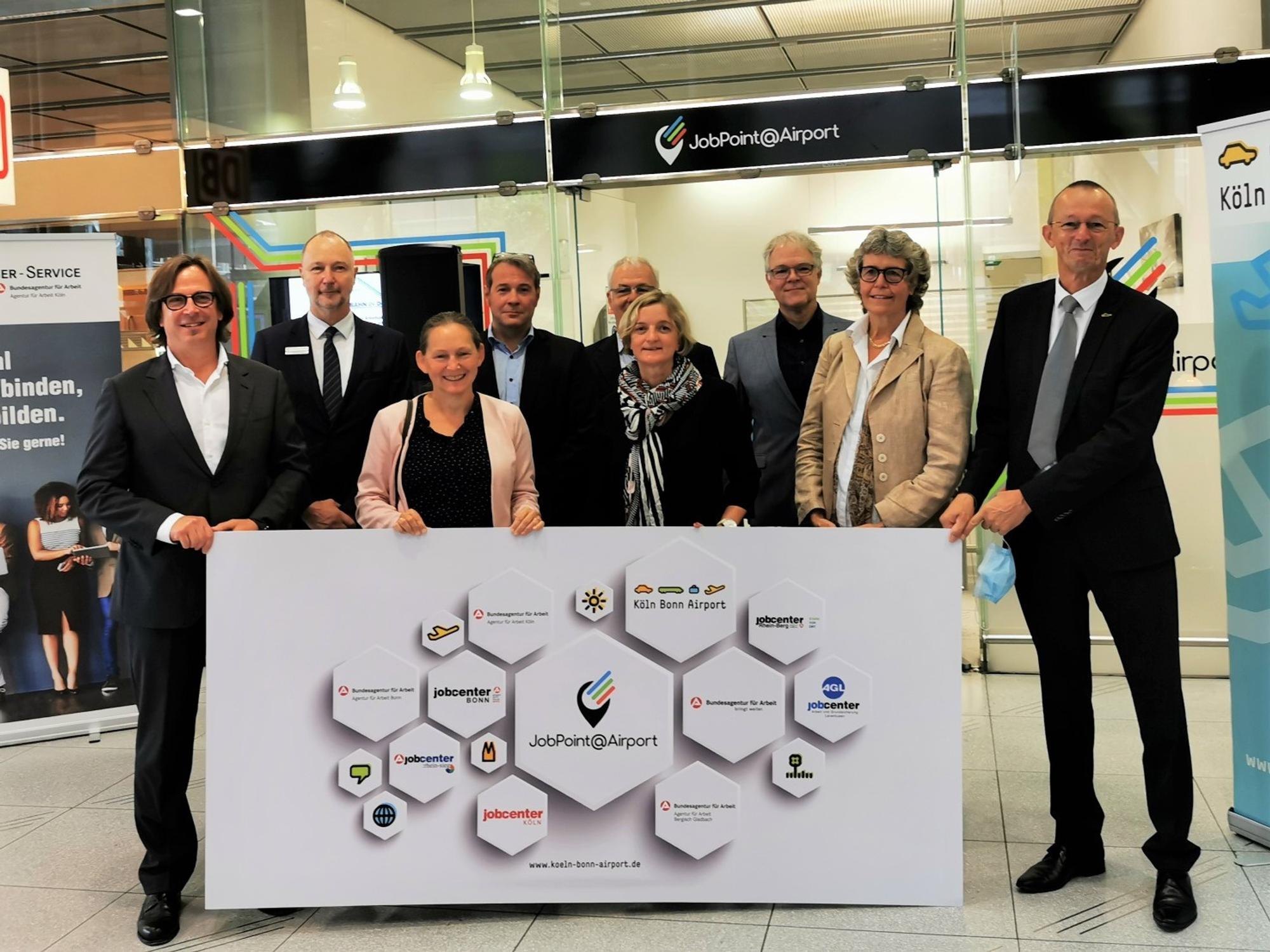 Die Gründer der neuen Zweigstelle der Agentur für Arbeit am Flughafen Köln/Bonn halten ein Plakat in die Höhe.