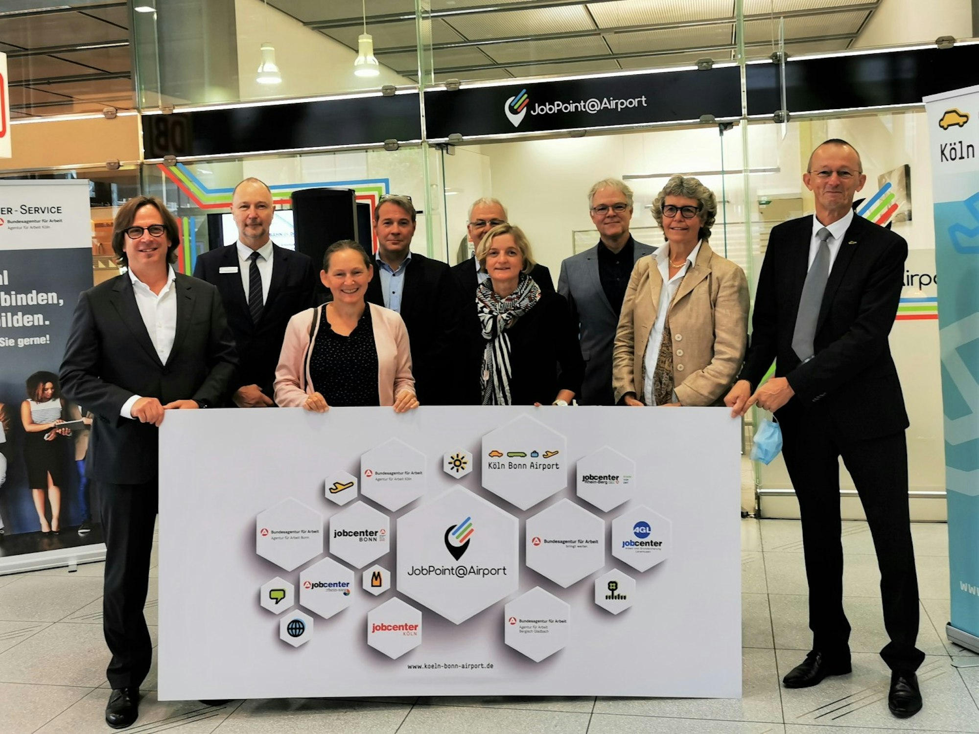 Die Gründer der neuen Zweigstelle der Agentur für Arbeit am Flughafen Köln/Bonn halten ein Plakat in die Höhe.