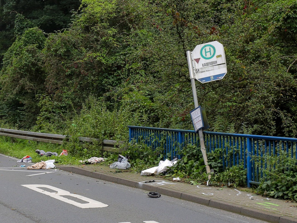 Das Schild einer Bushaltestelle ist umgebogen, ein kleines Rad und andere Gegenstände liegen davor verstreut.