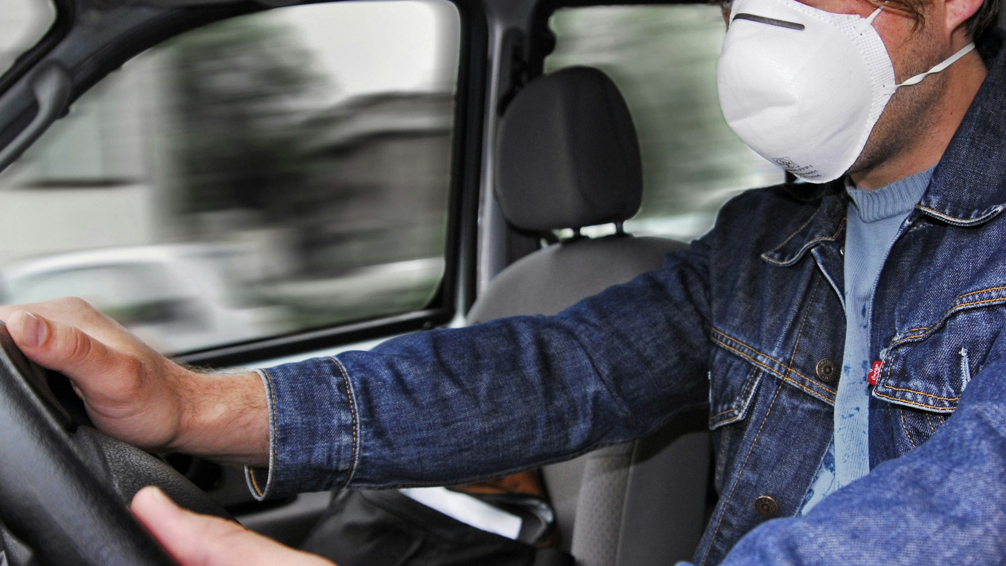 Ein Mann sitzt in unserem Symbolbild mit Corona-Mundschutz am Autosteuer: Ein betrunkener Fahrer ist in Ahlen in das Auto einer Frau gefahren und hat sie schwer verletzt. Nach einer dreisten Lüge flüchtete er.