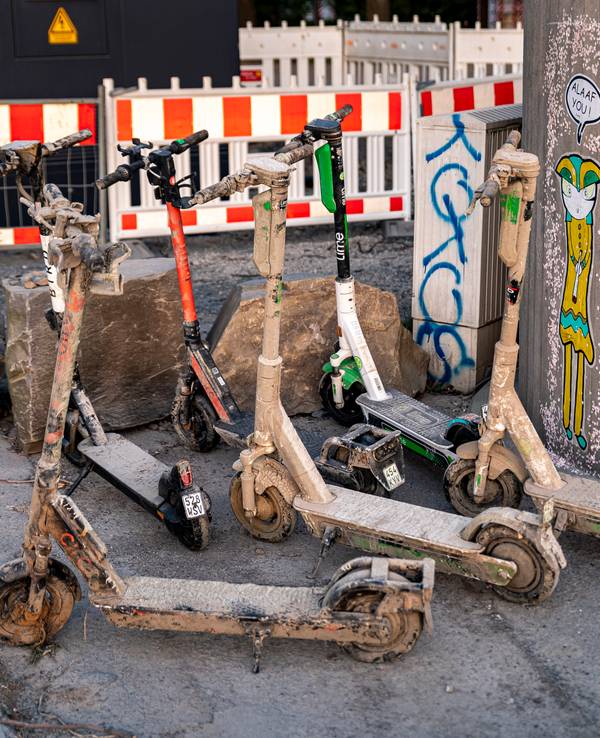 Verschlammte E-Scooter stehen an einer Mauer in Köln.