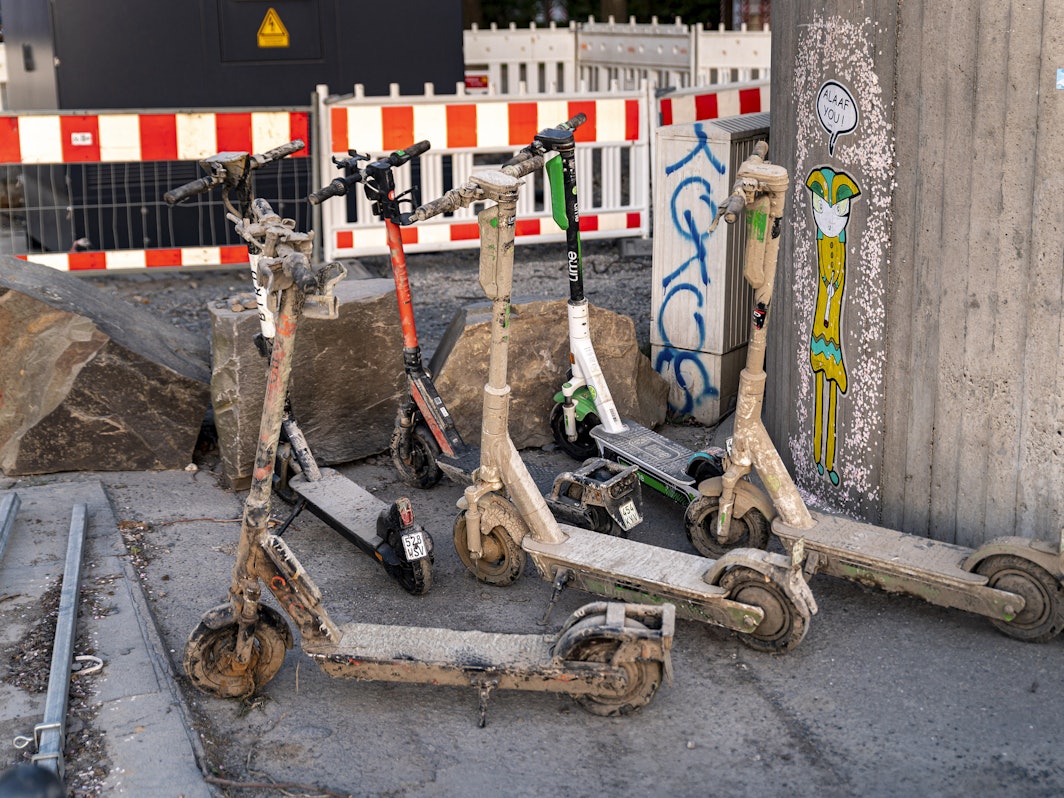 Mit getrocknetem Schlamm und Schmutz bedeckte E-Scooter stehen an einer Mauer.
