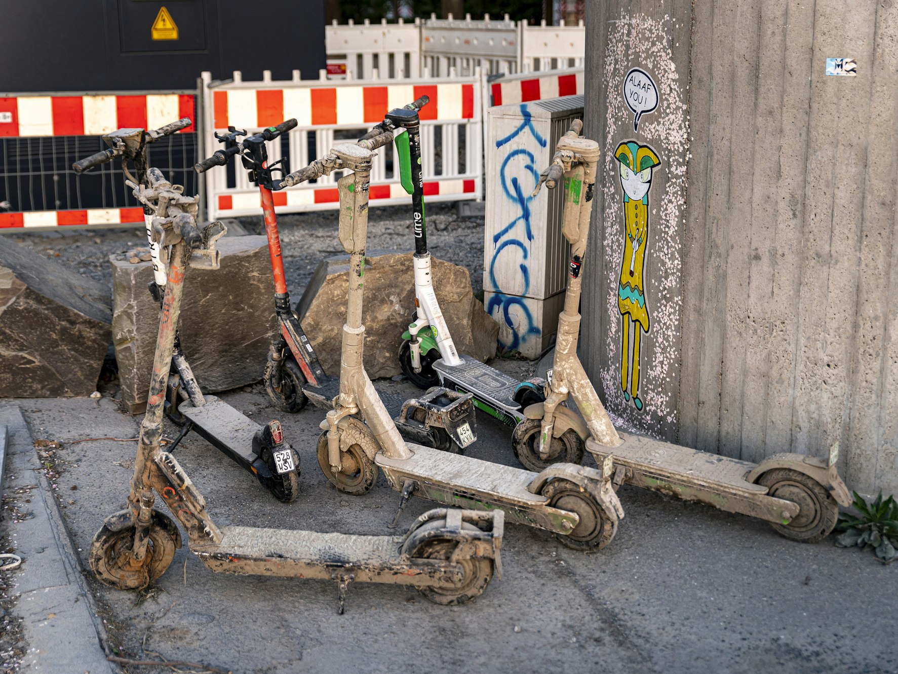 Verschlammte E-Scooter stehen an einer Mauer in Köln.