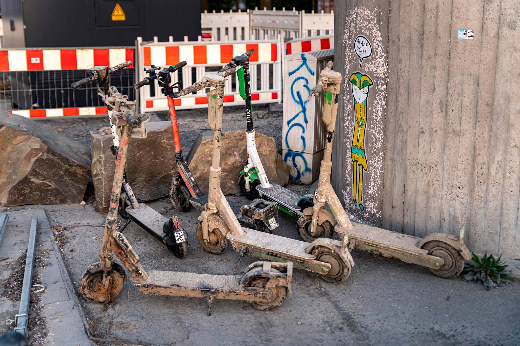 Mit getrocknetem Schlamm und Schmutz bedeckte E-Scooter stehen an einer Mauer.