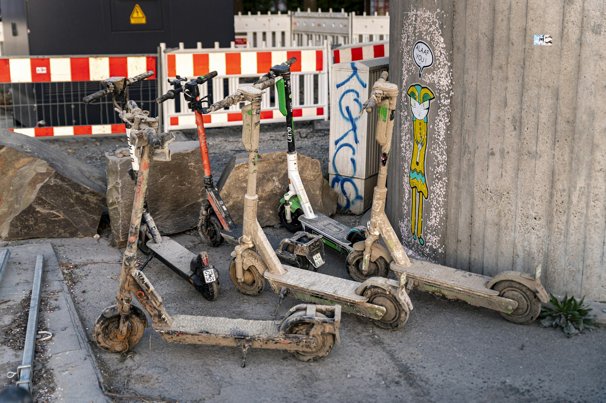Mit getrocknetem Schlamm und Schmutz  bedeckte E-Scooter stehen an einer Mauer.