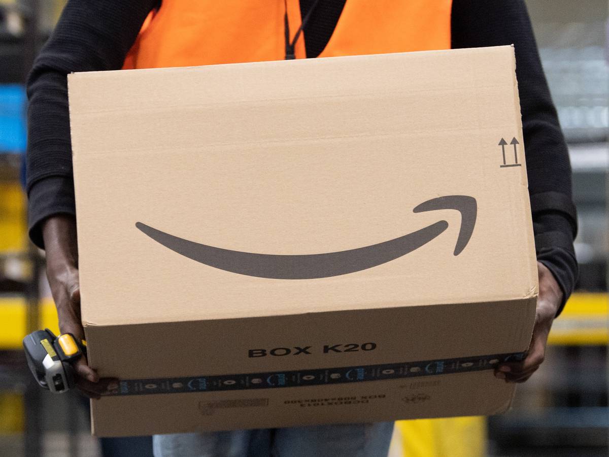 Ein Sortiermitarbeiter von Amazon trägt in einem Verzeilzentrum ein Paket.