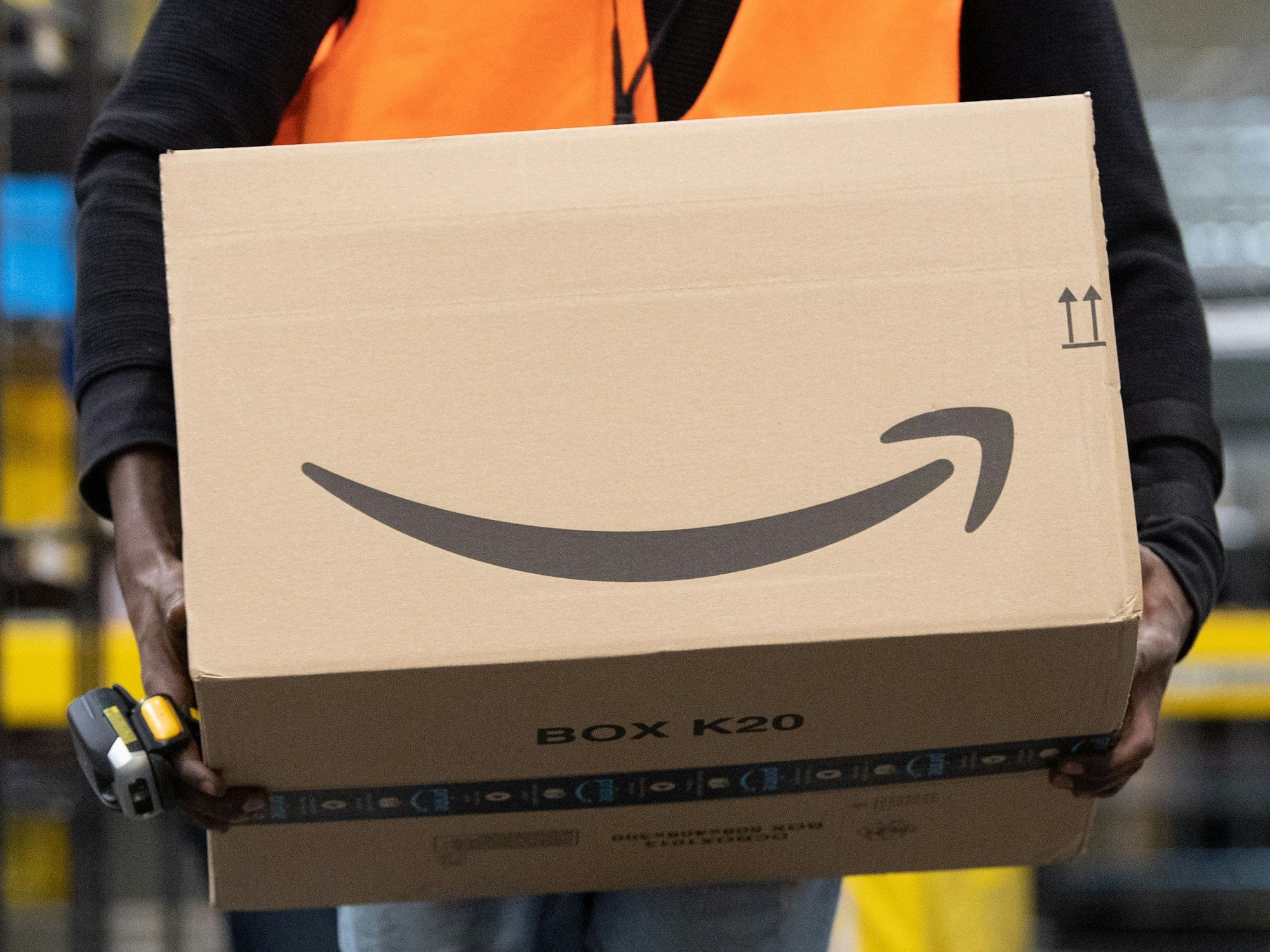 Ein Sortiermitarbeiter von Amazon trägt in einem Verzeilzentrum ein Paket.