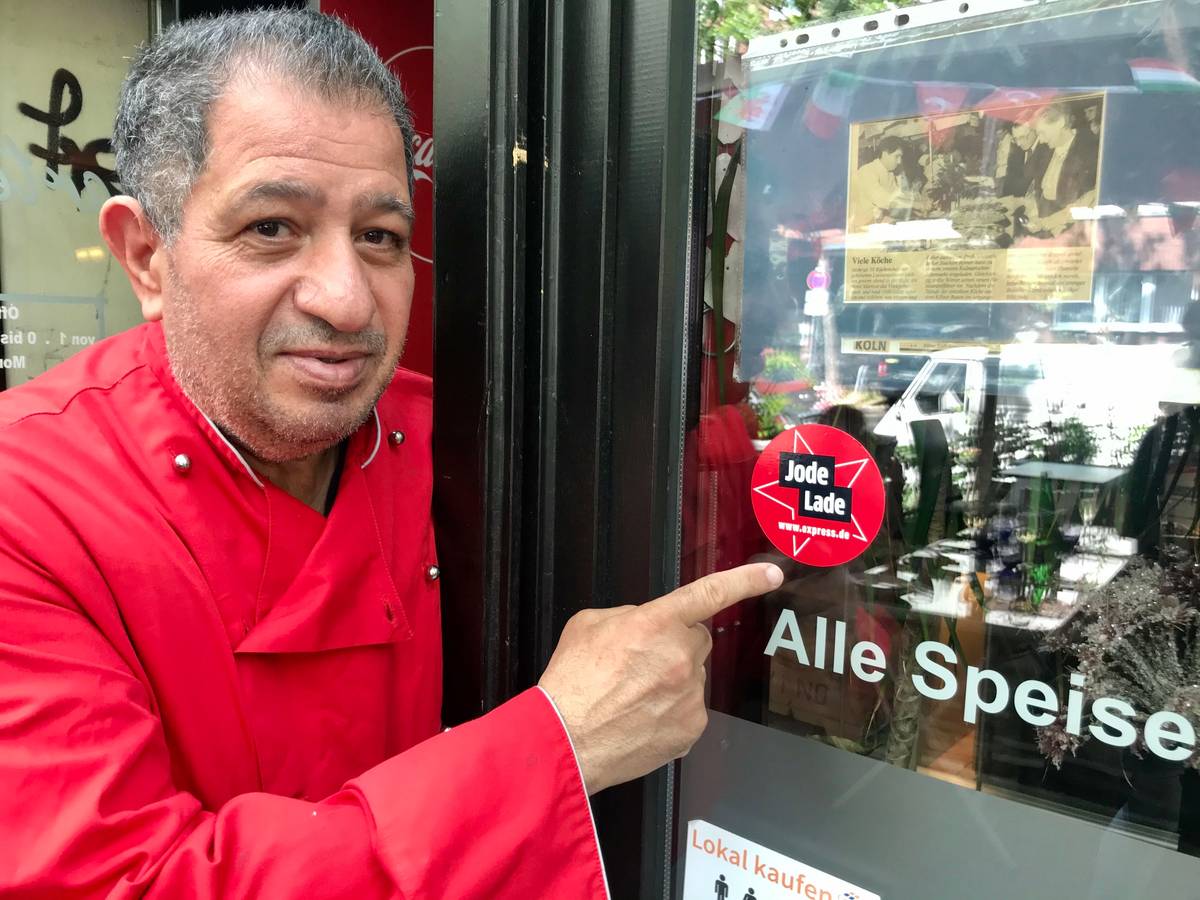 Carmelo Faraci zeigt auf den Jode-Lade-Aufkleber auf der Fensterscheibe des Lokals.