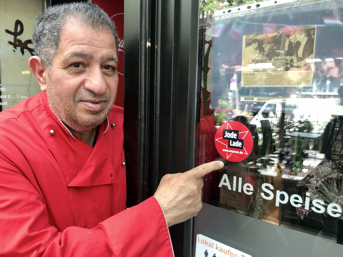 Carmelo Faraci zeigt auf den Jode-Lade-Aufkleber auf der Fensterscheibe des Lokals.