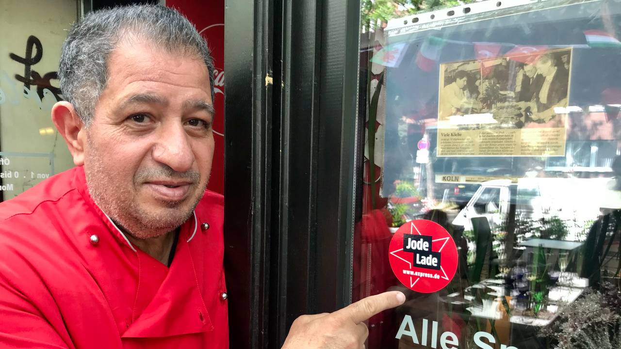 Carmelo Faraci zeigt auf den Jode-Lade-Aufkleber auf der Fensterscheibe des Lokals.