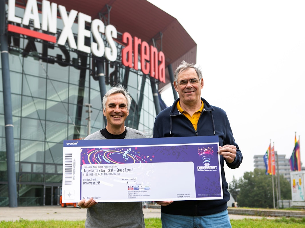 Ein Jahr vor dem Turnierstart: Die Kölner Basketball-Legenden Stefan Baeck und Klaus Zander präsentieren ein symbolisches Ticket für die Basketball-EM 2022 in Köln und Berlin.