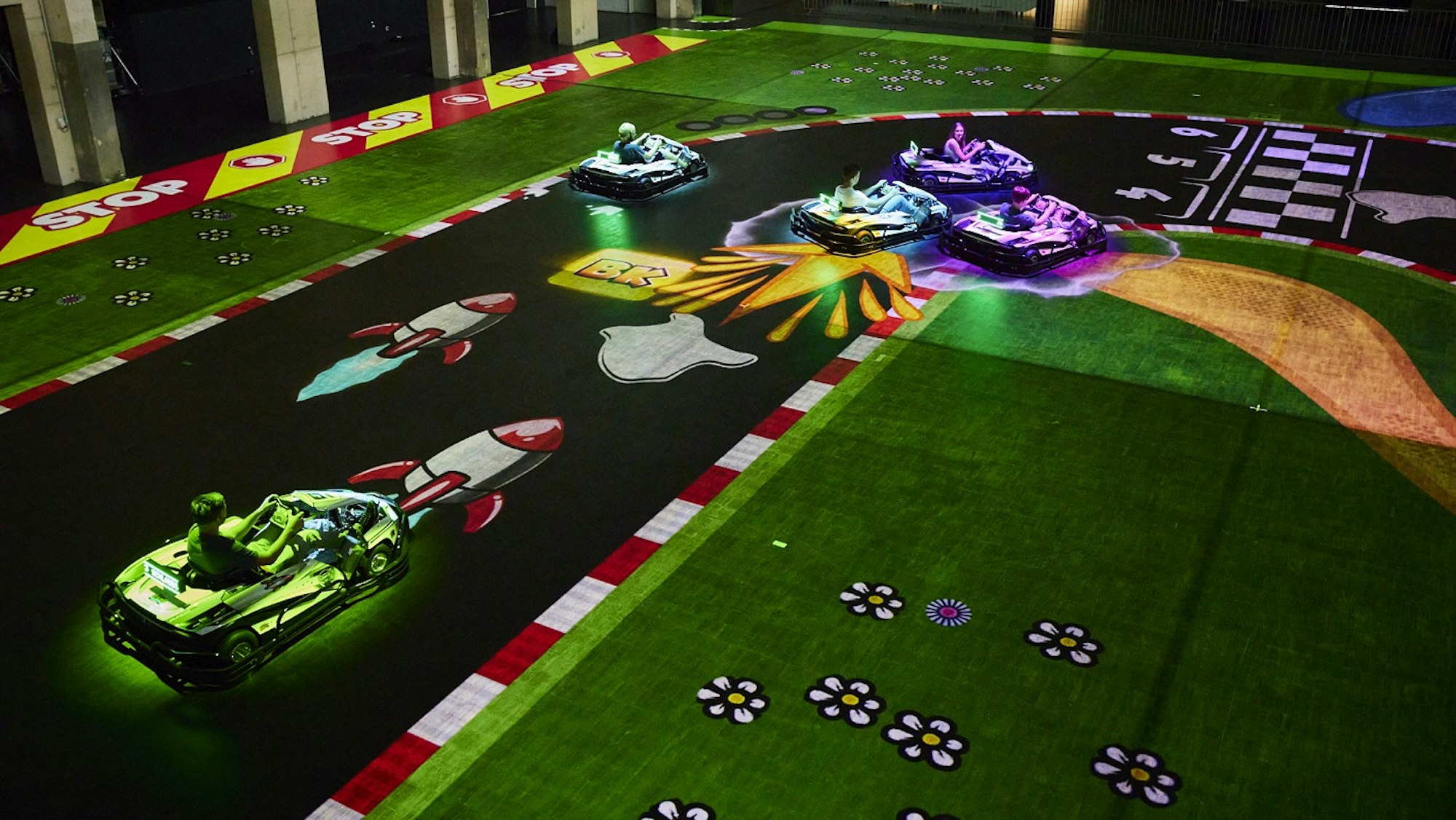 Fünf Elektro-Karts fahren auf einer auf den Boden projizierten Strecke.