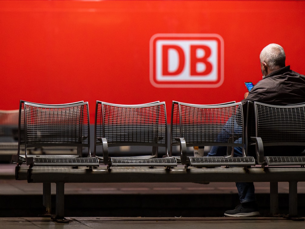 Das Logo der Deutschen Bahn (DB) prangt an der Seite einer Lok, während ein Mann in München am Donnerstag (2. September) auf dem Hauptbahnhof wartet. Die Deutsche Bahn geht gerichtlich gegen den GDL-Streik vor.