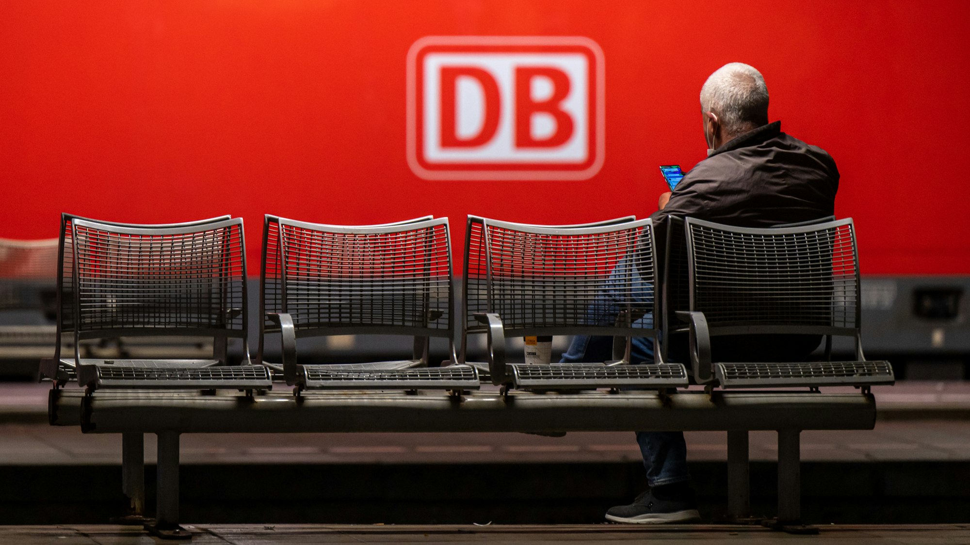 Das Logo der Deutschen Bahn (DB) prangt an der Seite einer Lok, während ein Mann in München am Donnerstag (2. September) auf dem Hauptbahnhof wartet. Die Deutsche Bahn geht gerichtlich gegen den GDL-Streik vor.