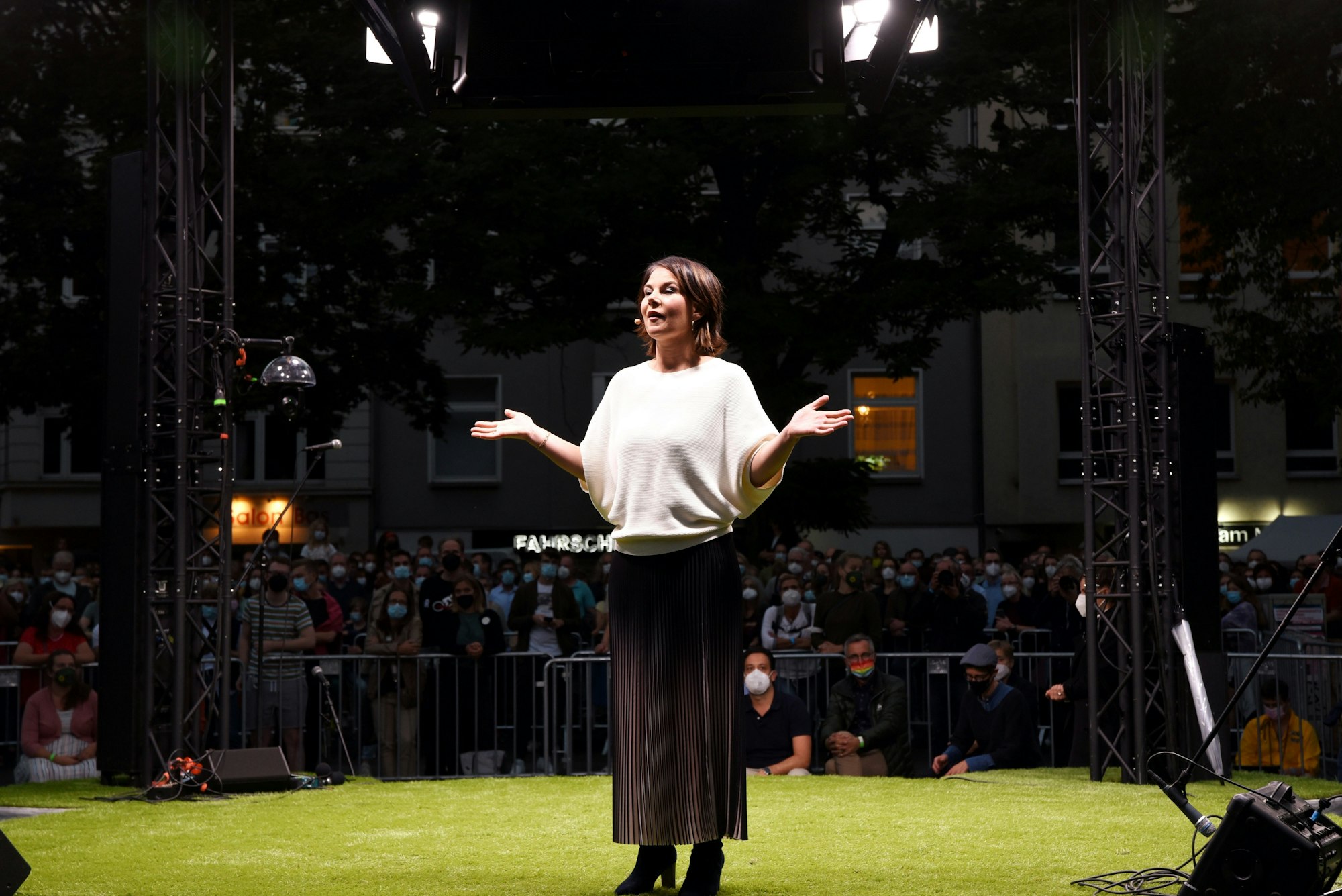 Annalena Baerbock spricht mit ausgebreiteten Armen auf grünem Kunstrasen.