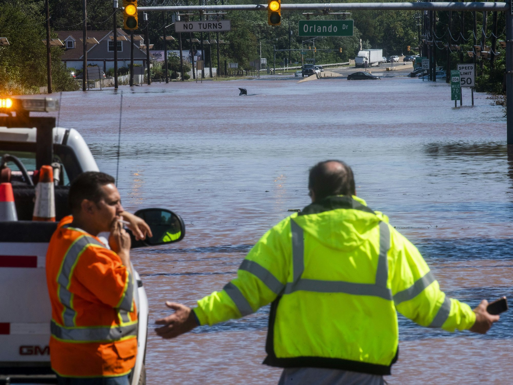 Menschen stehen an der überfluteten Bundesstraße 206 in New Jersey. Im Hintergrund sind überflutete Autos zu sehen.