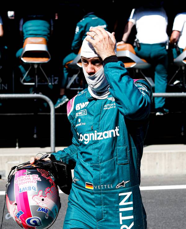 Sebastian Vettel mit Helm in der Hand und Gesichtsmaske auf dem Kopf fasst sich an den Kopf.