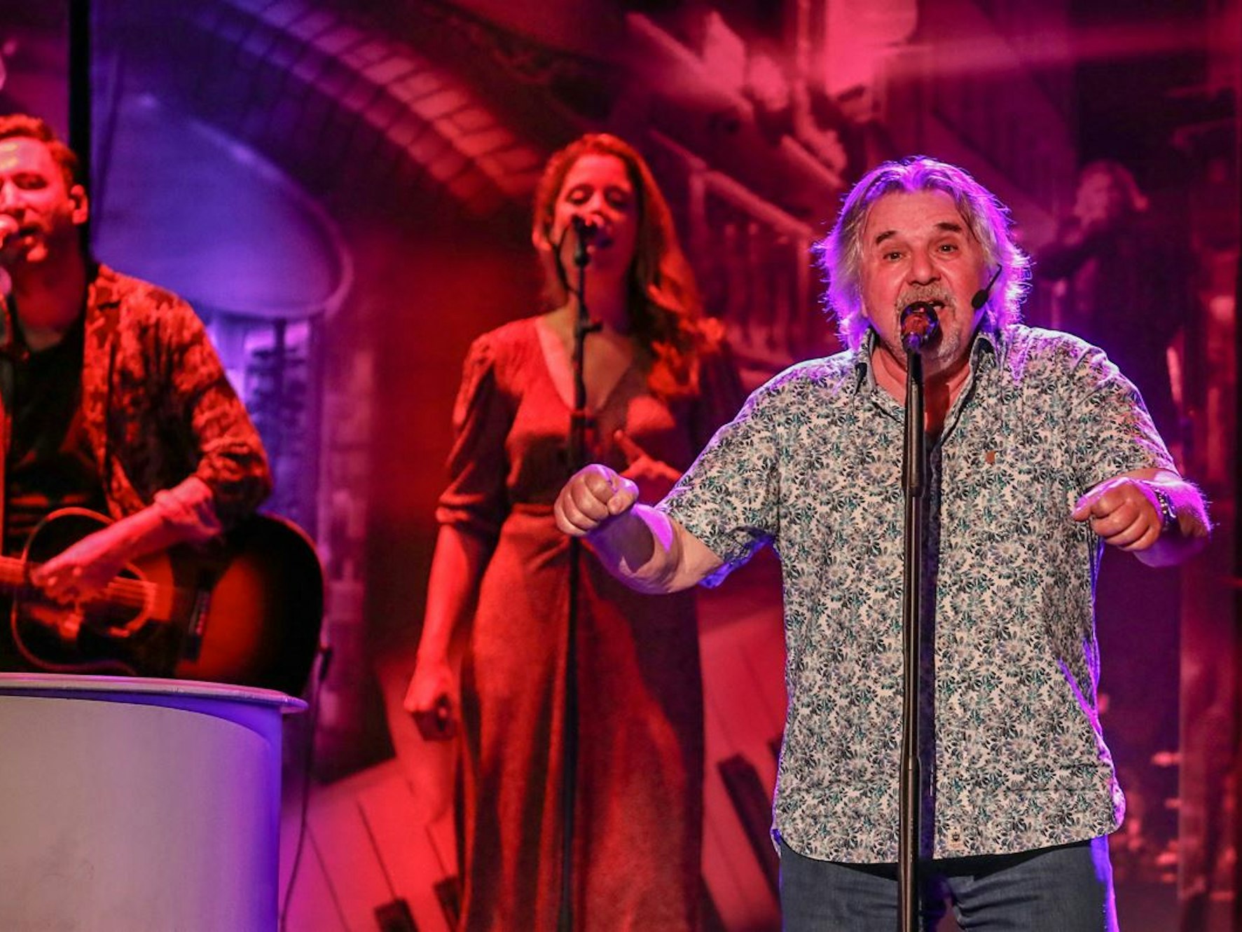 Tommy Engel steht auf einer Bühne vor einem Mikrofon bei einem Konzert.