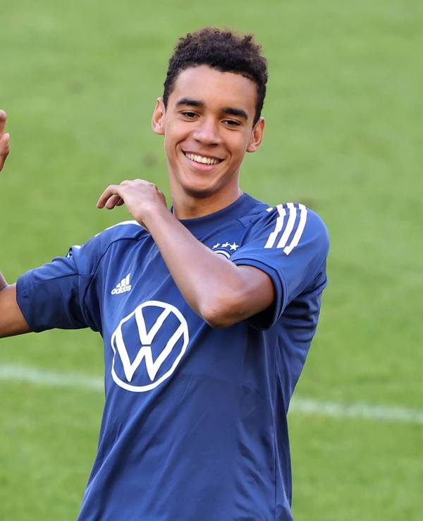Jamal Musiala steht lachend auf dem Platz