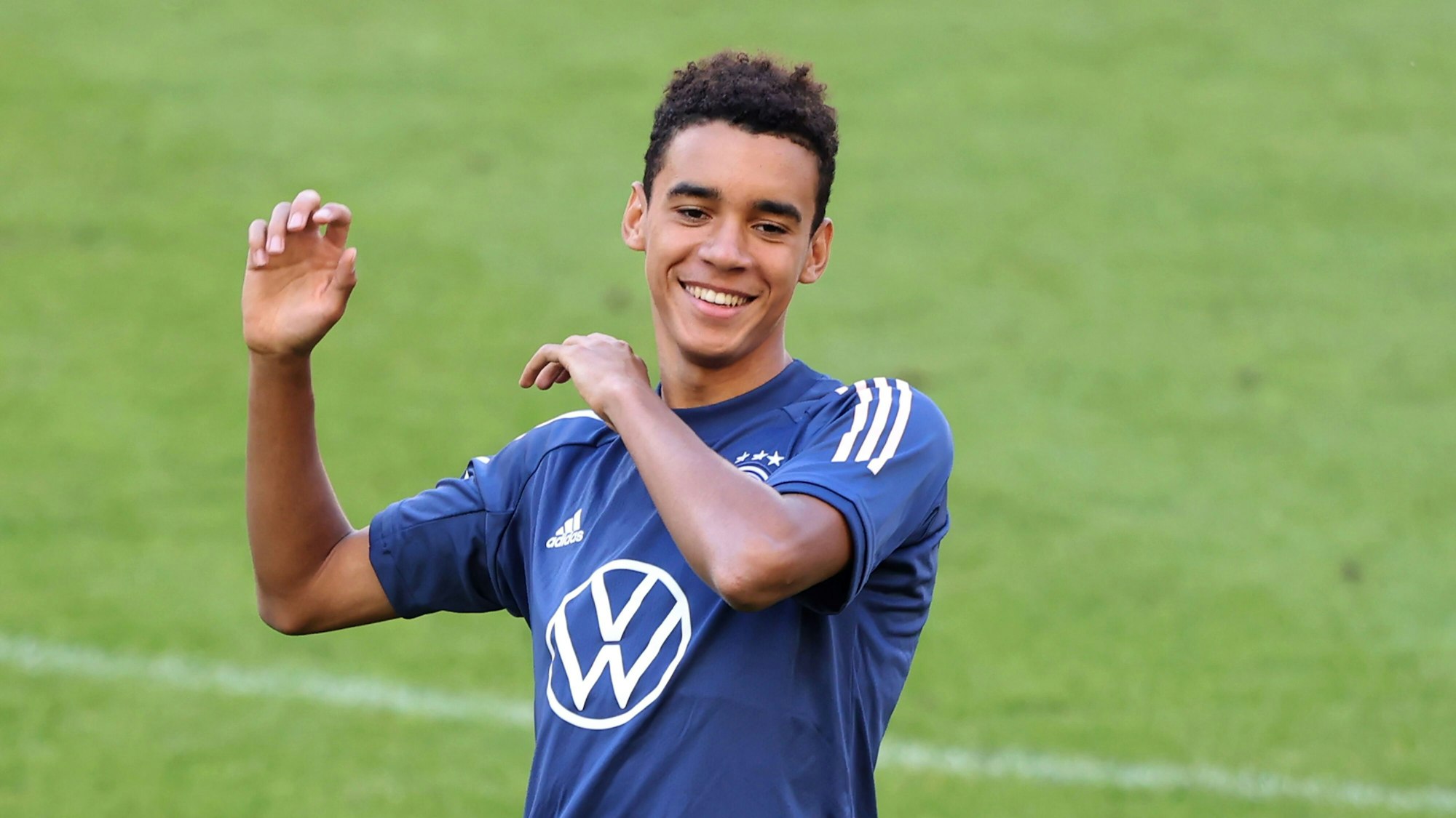 Jamal Musiala steht lachend auf dem Platz