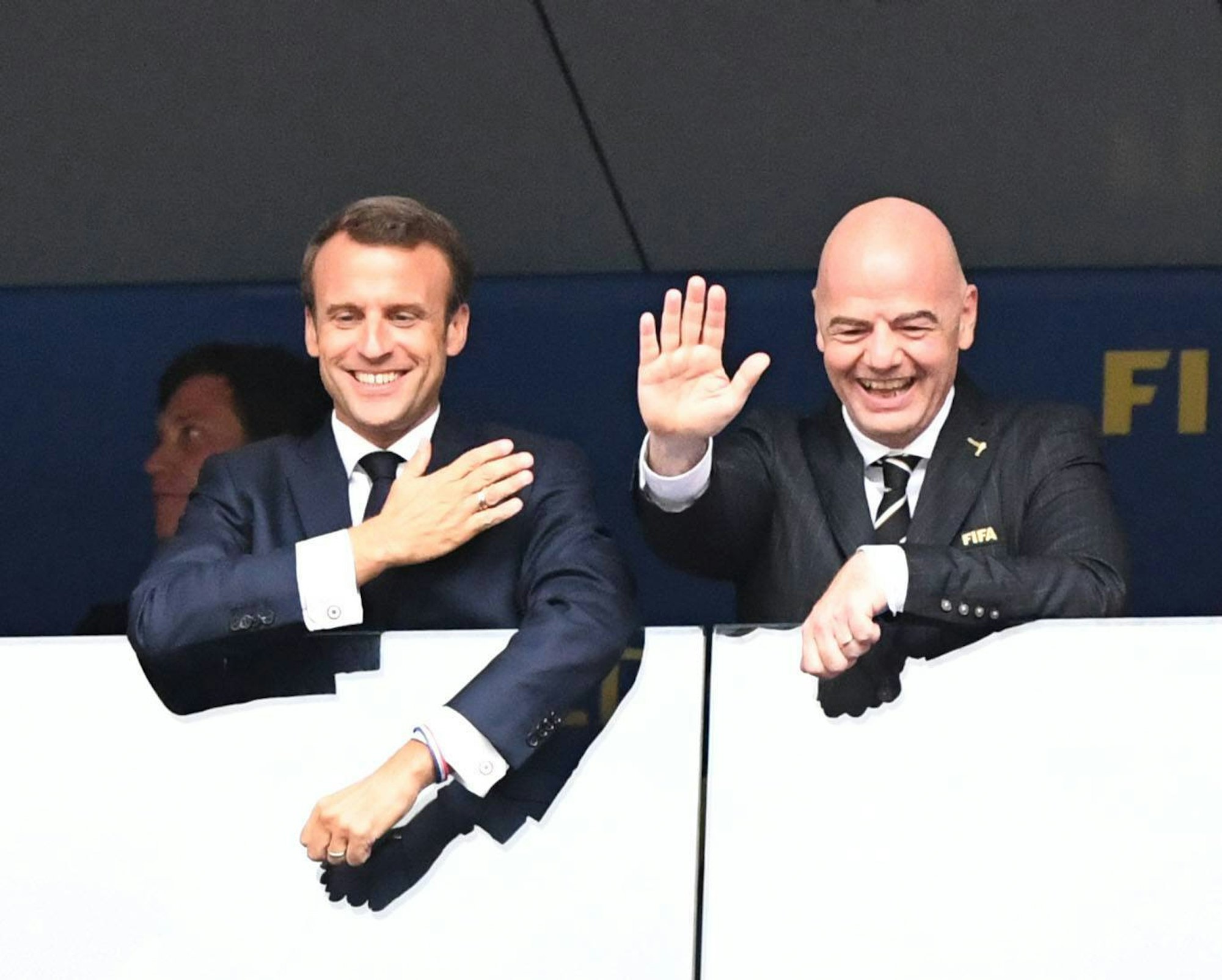 Frankreichs Präsident Macron steht an der Seite von FIFA-Boss Infantino. Infantino winkt.