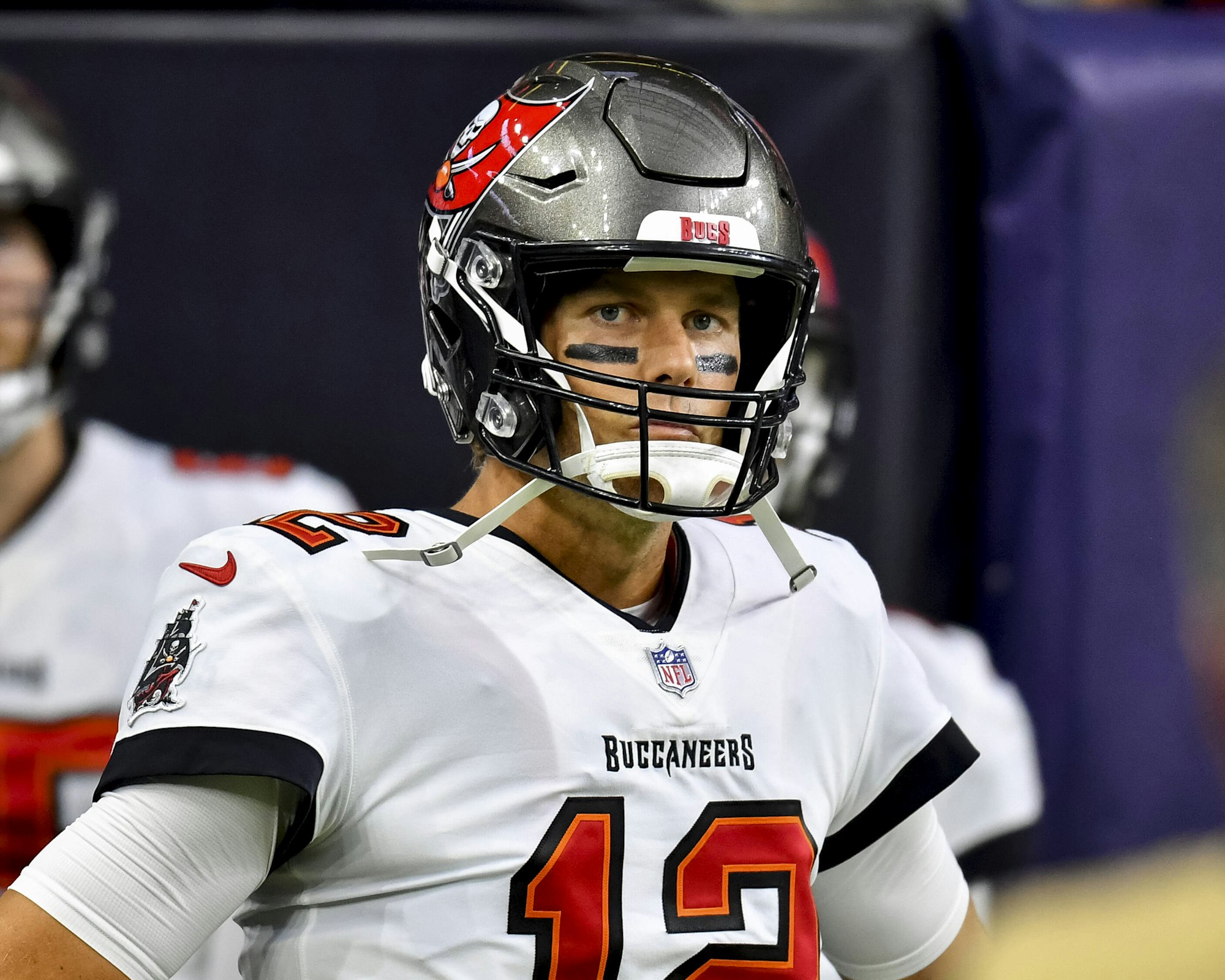 Tom Brady, mit Helm, Trikot und schwarz untermalten Augen, guckt in die Kamera.