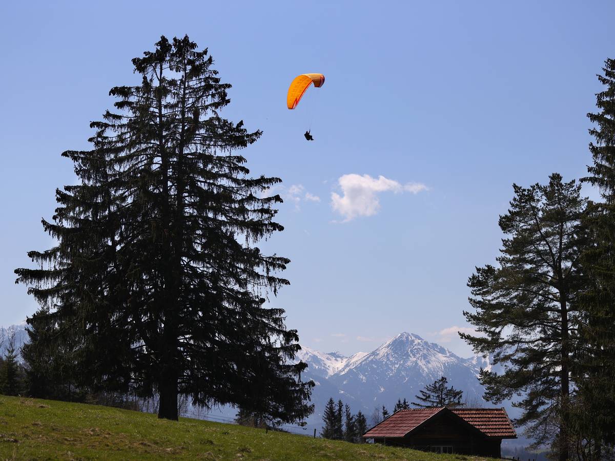 Ein Gleitschirmflieger über einer Hütte in Bayern.