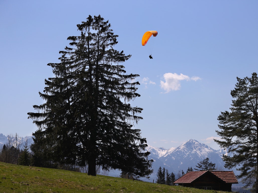 Ein Gleitschirmflieger über einer Hütte in Bayern.