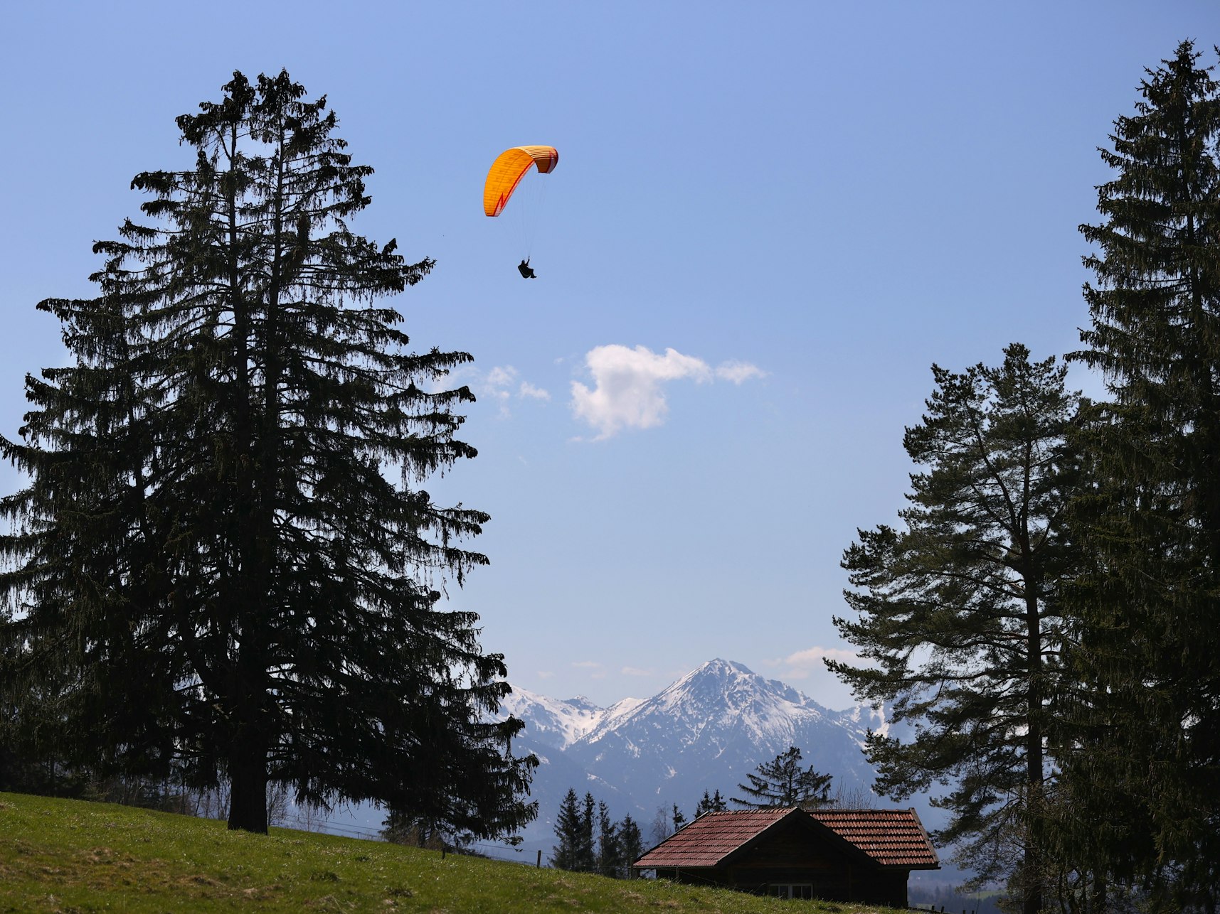 Ein Gleitschirmflieger über einer Hütte in Bayern.