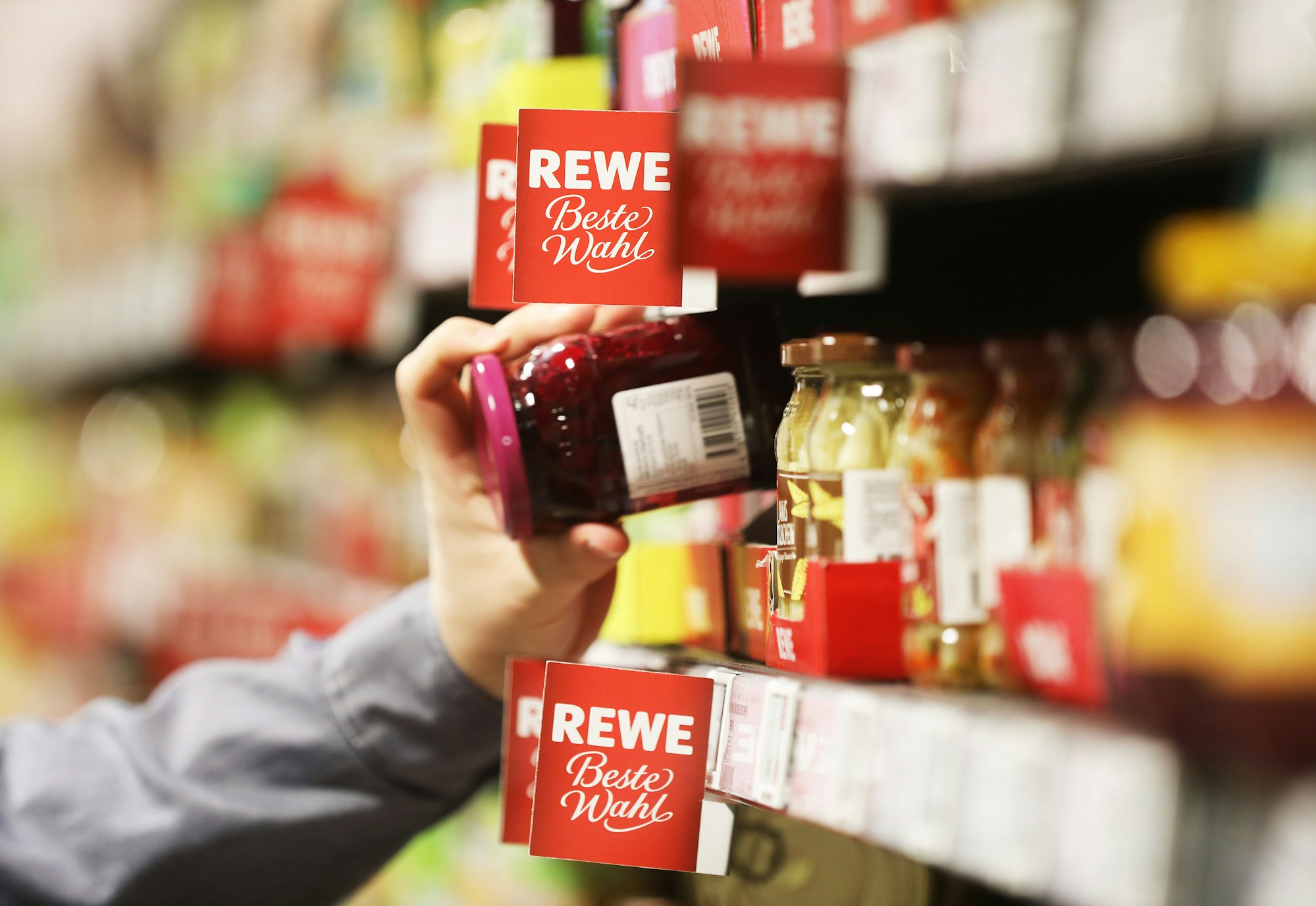 Ein Mann nimmt in unserem Symbolbild ein Glas aus dem Regal einer Rewe-Filiale. Vielerorts sind wieder Weihnachtsprodukte erhältlich, die Kundschaft zeigt sich auf Twitter gespalten.
