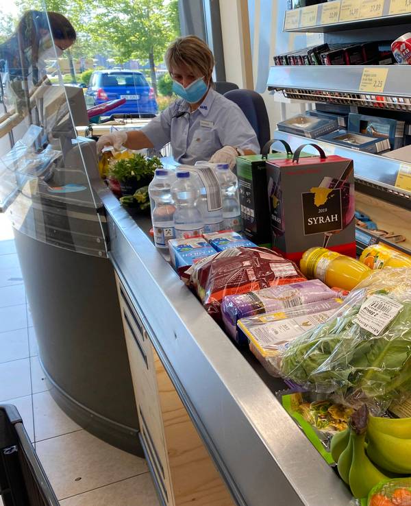 Unser Symbolfoto vom 20. Mai 2020 zeigt eine ALDI-Kassiererin mit Mund-Nase-Bedeckung, die Artikel vom Kassenband scannt. Neben ihr steht eine Kundin.