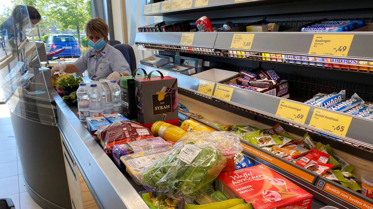 Unser Symbolfoto vom 20. Mai 2020 zeigt eine ALDI-Kassiererin mit Mund-Nase-Bedeckung, die Artikel vom Kassenband scannt. Neben ihr steht eine Kundin.