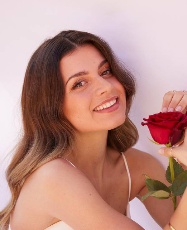 „Bachelorette“ Maxime lächelt in die Kamera und hält eine Rose in der Hand.
