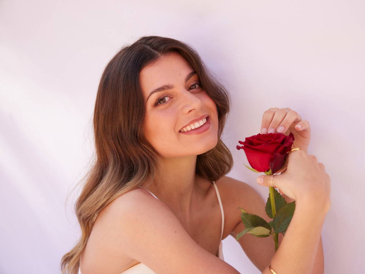 „Bachelorette“ Maxime lächelt in die Kamera und hält eine Rose in der Hand.