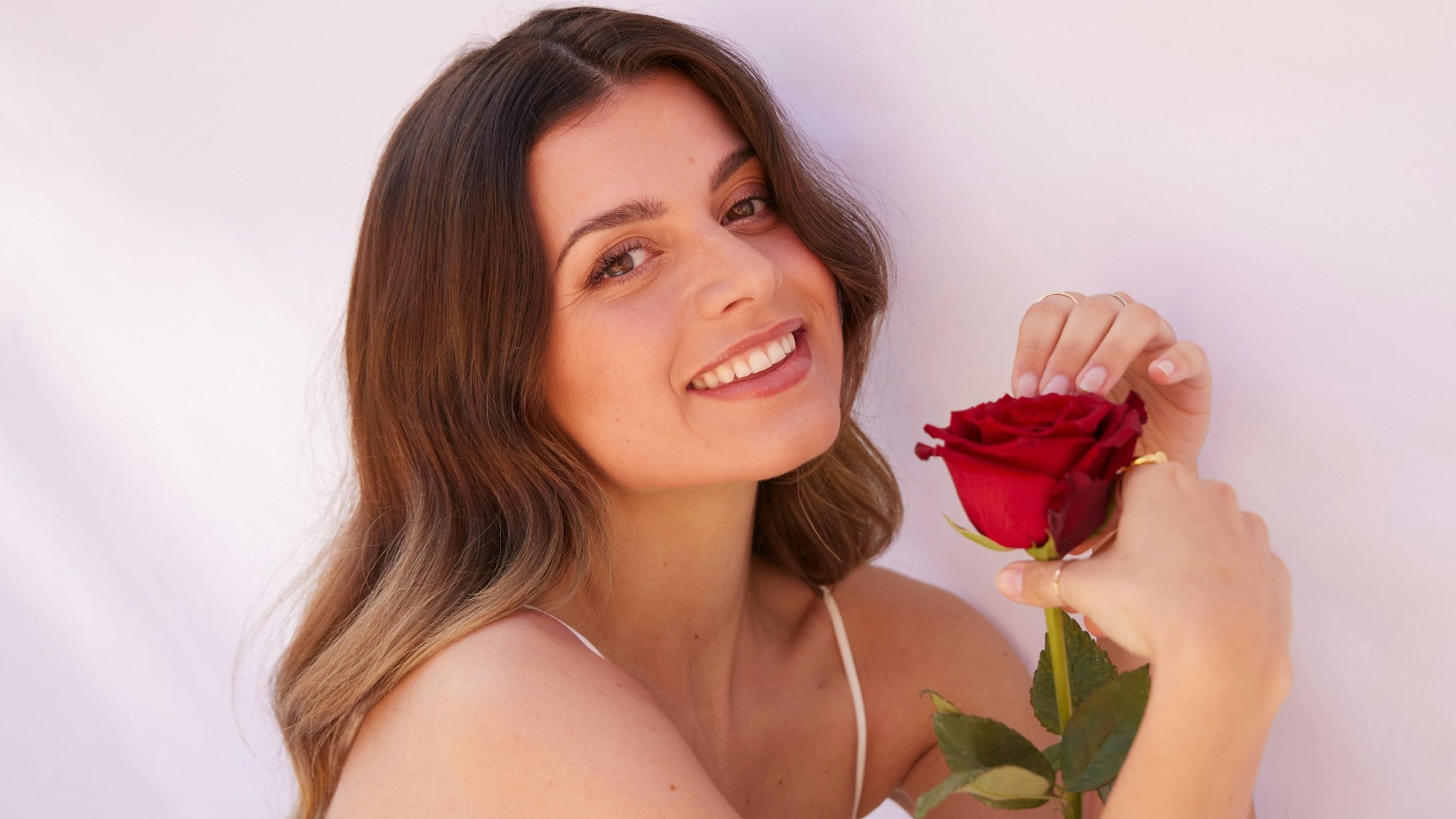 „Bachelorette“ Maxime lächelt in die Kamera und hält eine Rose in der Hand.