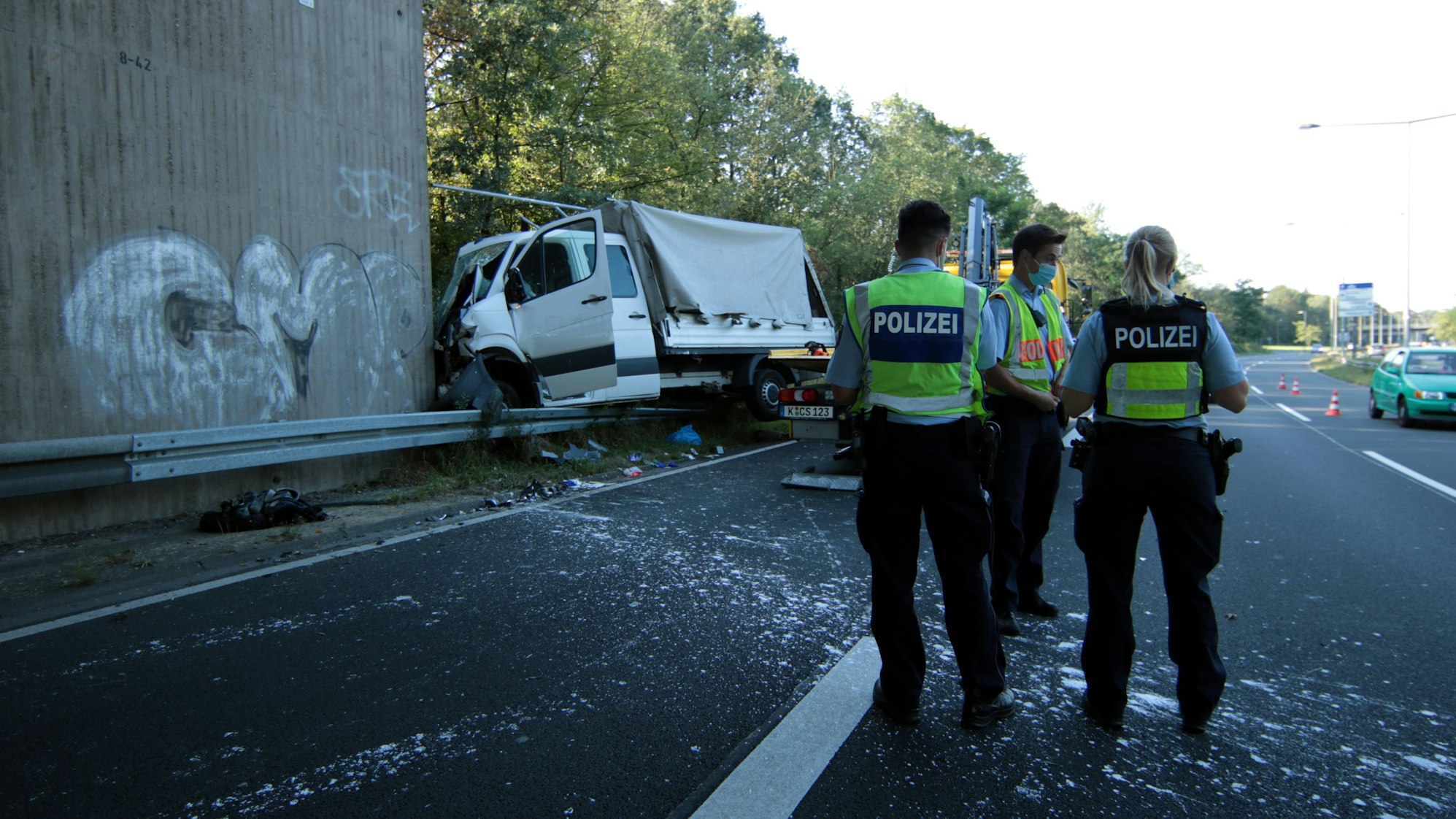Drei Polizisten stehen auf der Fahrbahn, ein paar Meter steht ein Kleinlaster schwer beschädigt an einer Mauer.