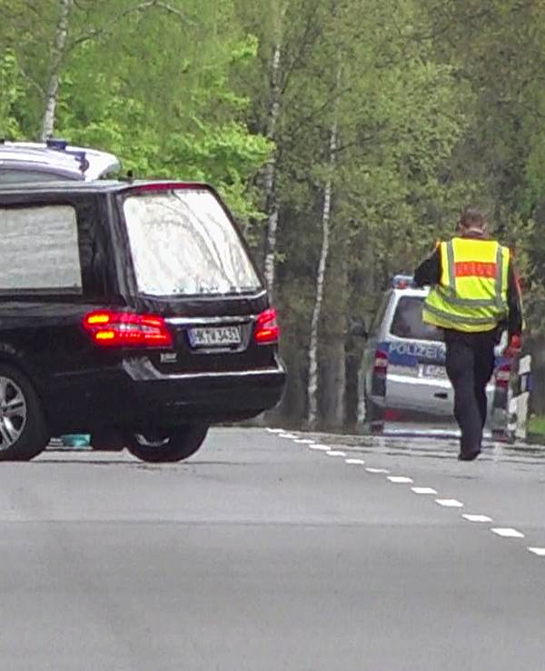 Ein Leichenwagen parkt an einer Straße vor Einsatzfahrzeugen der Polizei.