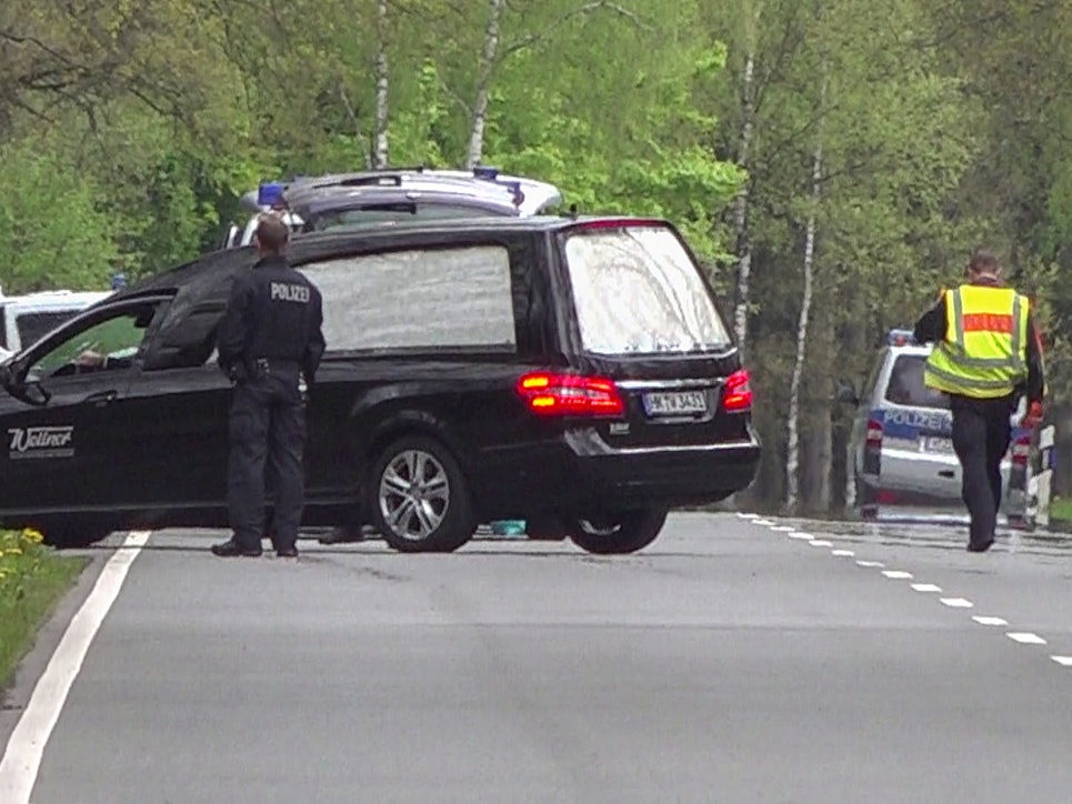 Ein Leichenwagen steht auf einer Straße, davor ein Polizist.