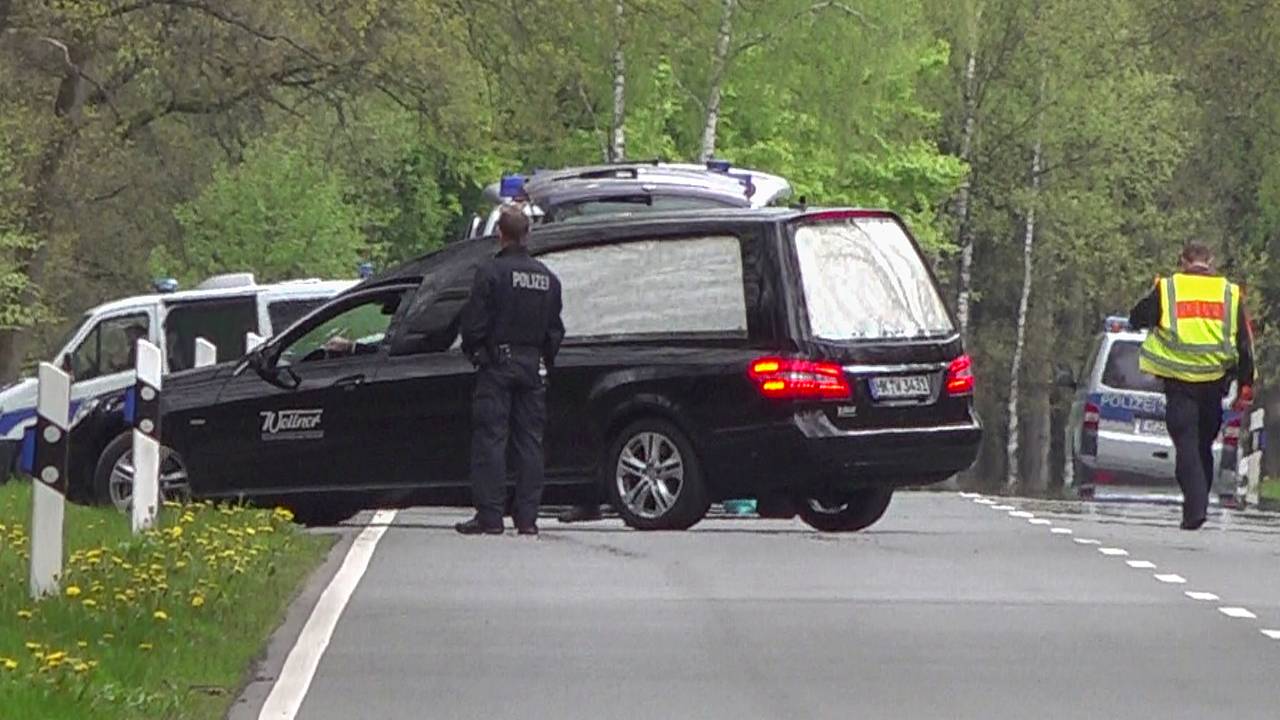 Ein Leichenwagen parkt an einer Straße vor Einsatzfahrzeugen der Polizei.